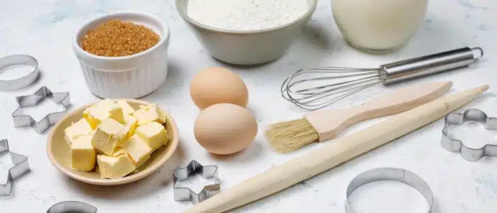 Displaying eggs, butter, flour, brown sugar, milk, and essential baking tools like whisk, brush, and cookie cutters, ideal setup for an expert kitchen baking ingredients guide
