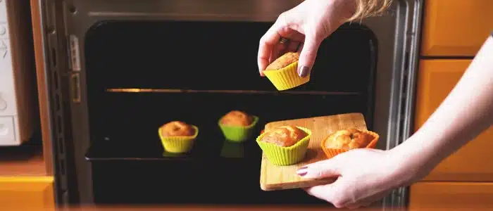 Displaying hands placing colorful muffin cups into a microwave oven, perfectly illustrating a beginner-friendly guide to microwave baking for home kitchens.
