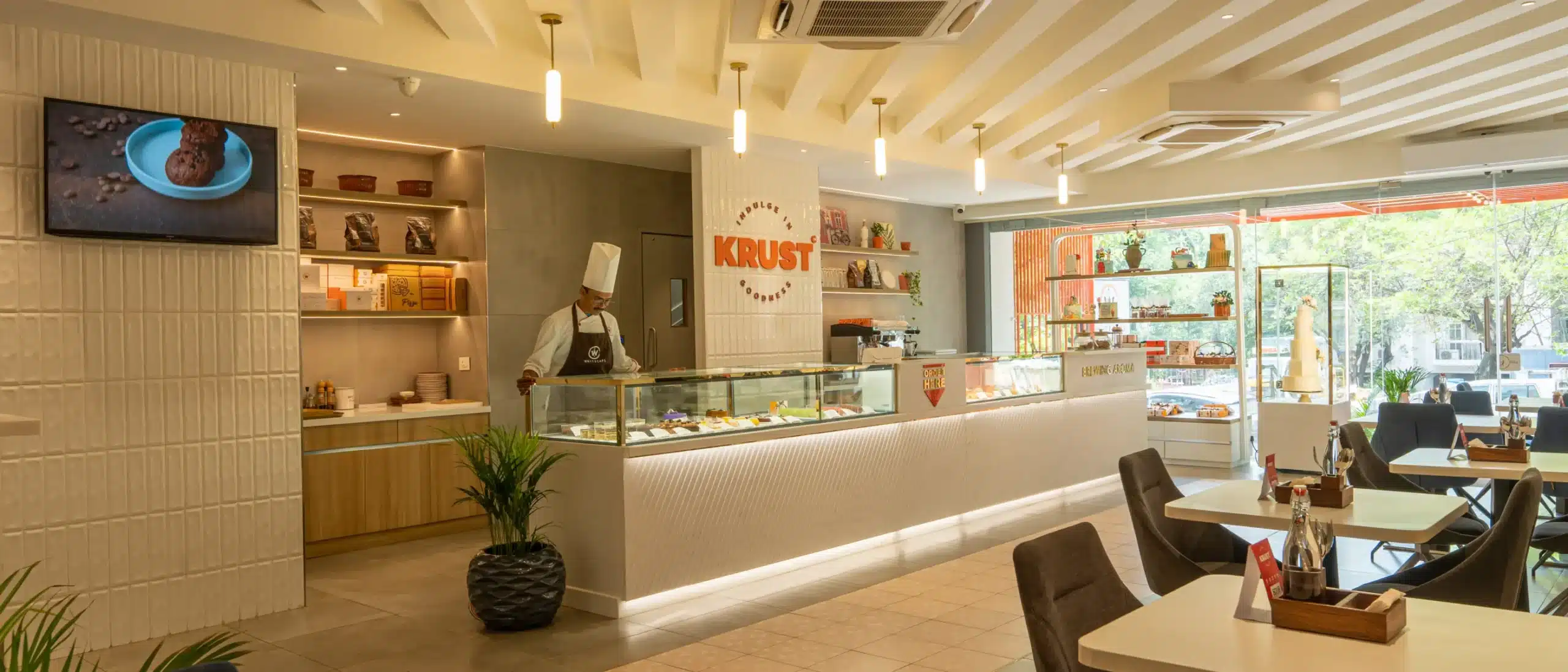 Displaying a modern bakery setup with a chef behind the counter, elegant interior design, pastry displays, and seating area, illustrating the ideal environment for starting a professional baking business