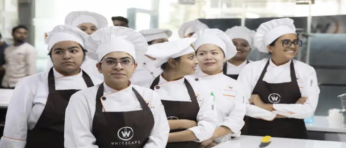 Group of professional baking students in chef uniforms and aprons at Whitecaps academy, standing in a modern training kitchen, symbolizing the next generation of bakers prepared to tackle key challenges in the bakery industry