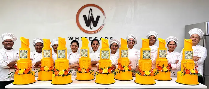 Chefs at Whitecaps standing behind bright yellow fondant cakes with floral decorations, showing the creative and colorful style of fondant cakes.